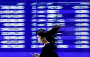 FILE PHOTO: A passerby walks past an electric monitor displaying recent movements of various stock prices outside a bank in Tokyo, Japan, March 22, 2023. REUTERS/Issei Kato/File Photo